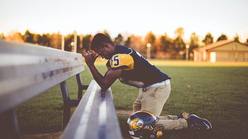 Football player kneeling, praying on bench seat