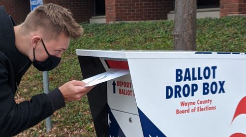 Man putting in mail-in vote in drop box with mask on