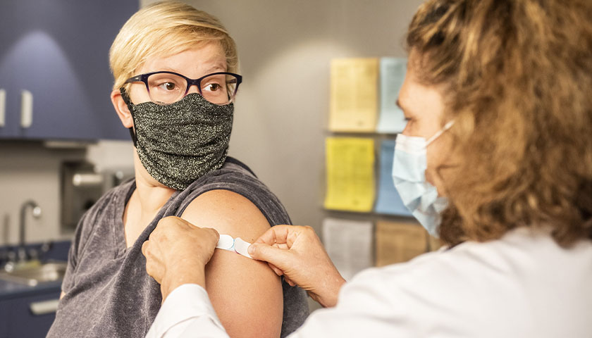 a health care provider places a bandage on the injection site of a patient, who just received a vaccine