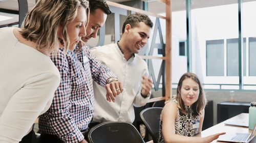 Group of people gathered, talking next to an office desk
