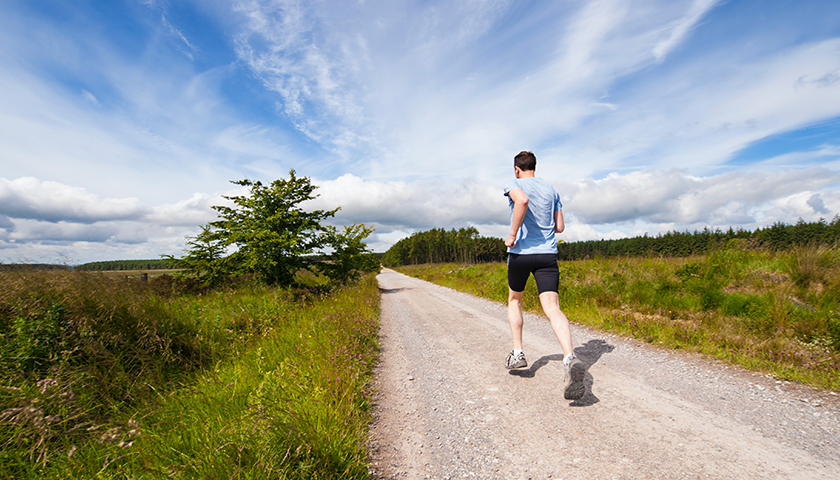 Man running on a gravel road during the day with a blue shirt on