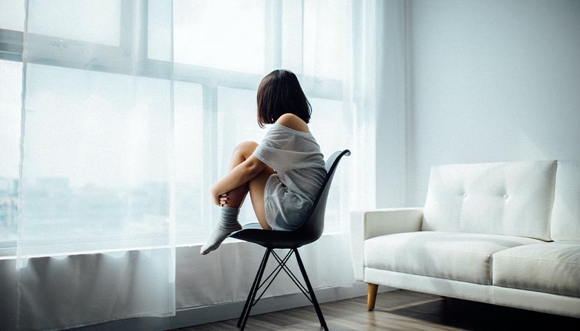 Woman sitting in a chair, looking out the window, alone
