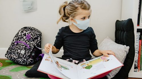 Young girl wearing a mask and reading a book in school