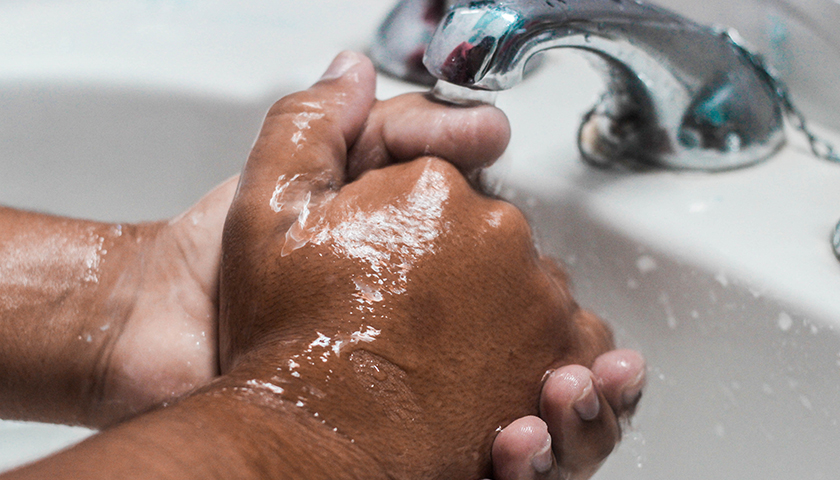 Close-up of person's hands being washed in a sink