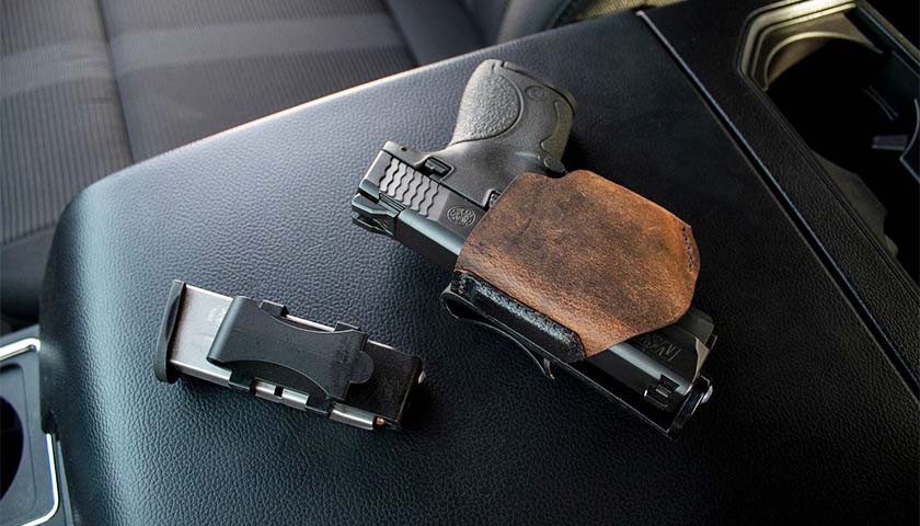 An unloaded handgun sitting on the center console of a vehicle with the magazine clip next to it