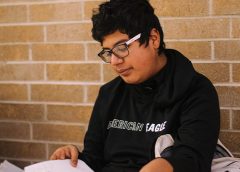 Young male with glasses, sitting in hallway going through paper
