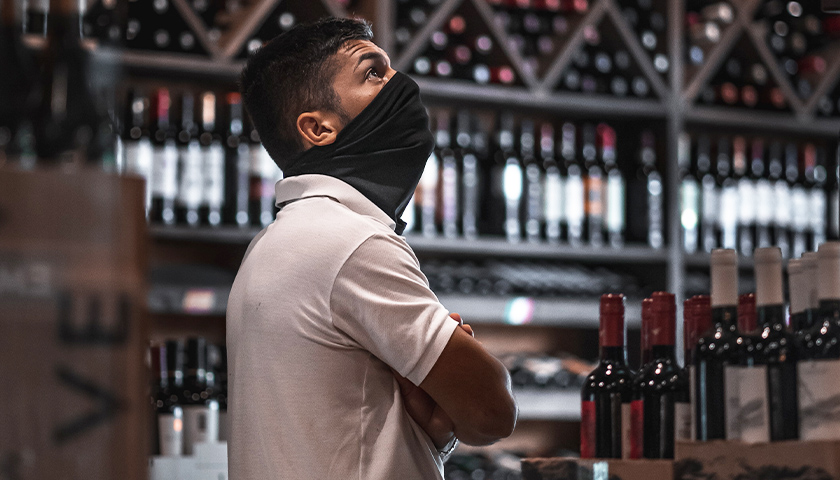 man standing next to wine bottles, wearing a mask
