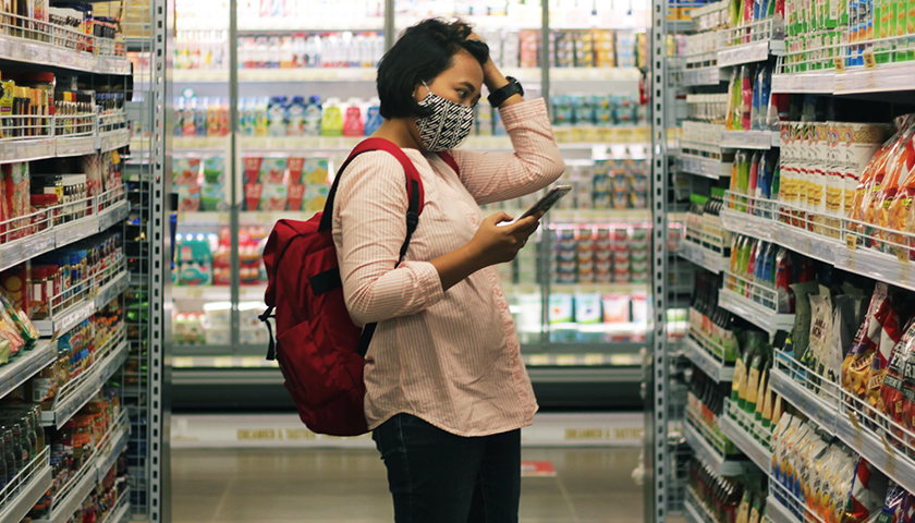 woman in a grocery aisle with a mask and backpack on