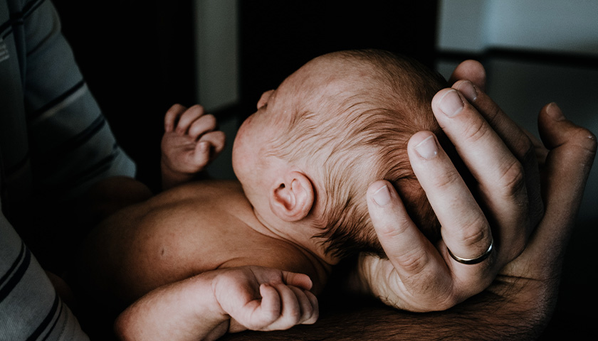 man's hand holding an infants head