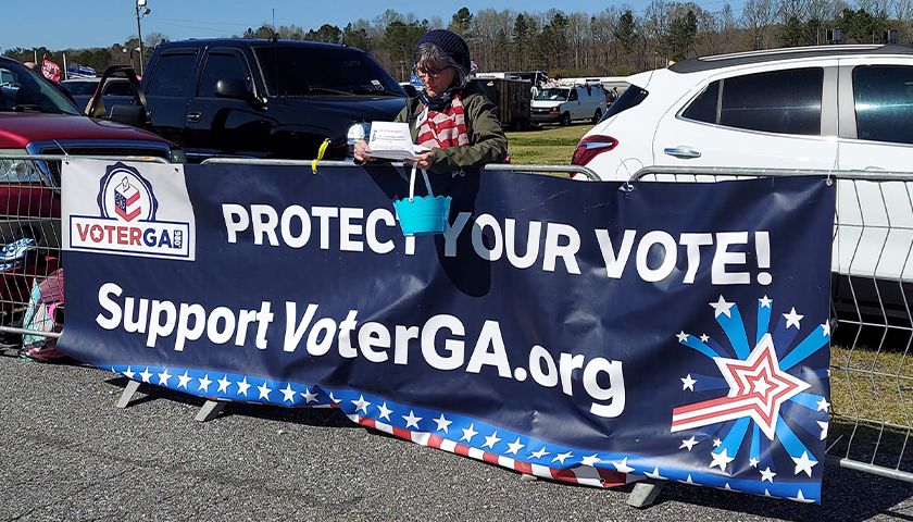 woman standing behind sign that says "protect your vote!"